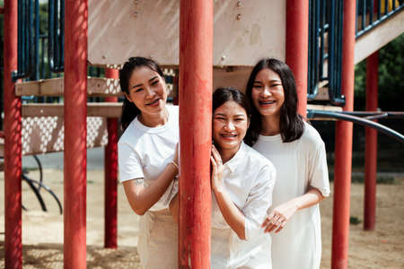 Triple twin sister happy at the red pole of plaything in the playground of the park.