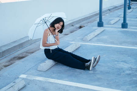 Sexy asian woman and umbrella sitting at parking lot. Thai woman resting at car park.の写真素材