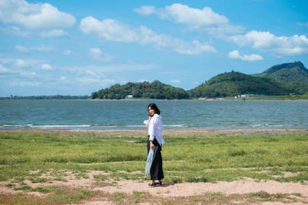 Cute young asian woman walking into lake holding umbrella. Sunny day.の写真素材