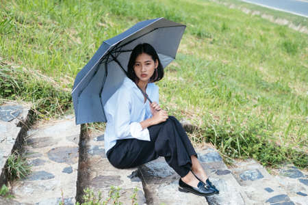 Cute young asian woman holding black umbrella sitting on a stair, rainning concept.の写真素材