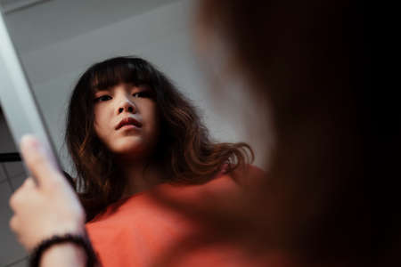 A Thai girl hold the mirror in her hand, her eye sight is empty 'cuase she cannot find the meaning of her life.の写真素材