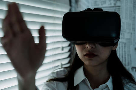 Front shot of woman in VR machine reach her hand out to the camera.