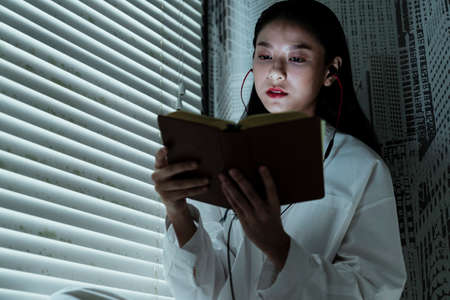 Low angle shot of woman in white clothes read the book at the window.の写真素材
