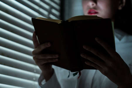 Cropped image of a book in woman's hand while she read it at the window.の写真素材