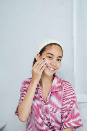 Long hair woman in red pajamas and headband wipe her face before cleaning, smile of happiness.の写真素材
