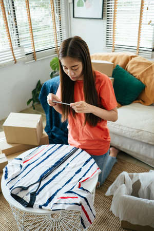 A woman in living room take a photo of pants that she received from online shop to write a review.の写真素材
