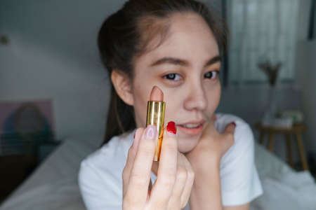 Ponytail woman show lipstick to the camera before apply on her lip while record the video.の写真素材