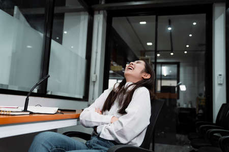 Black long hair podcaster girl in white shirt sitting on the chair after broaadcast and laugh.