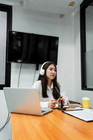 Black long hair podcaster girl in white shirt wearing white headphone grab the microphone on table...