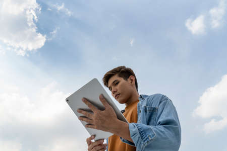 Asian thai man using tablet to connect the world. Man using tablet under blue sky.