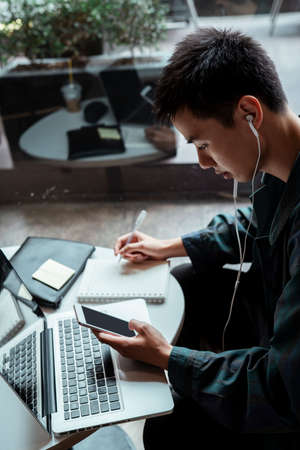 Short hair guy read a message from client and take a note into his notebook.