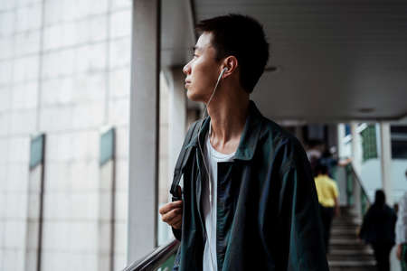 Short hair guy walking out og the shopping mall to the skywalk with earphone in his ear.の写真素材