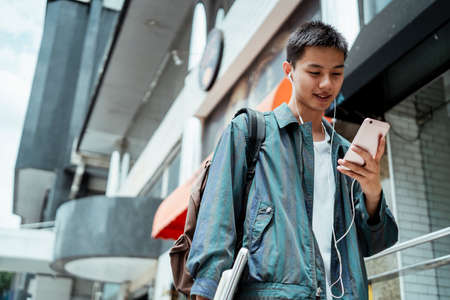 Low angle shot of short hair guy in jacket holding smartphone and find the correct bike from transportation application.の写真素材