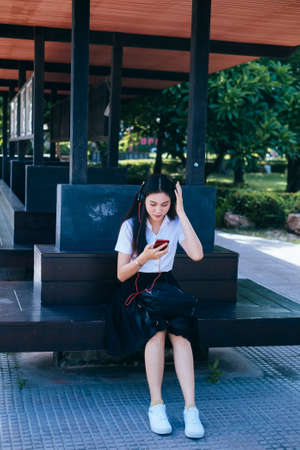 Black long hair college student girl sitting at the bench in university and listen the music from...