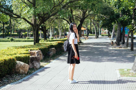 Black long hair college girl in uniform stop walking and turn to the camera while listen the music with headphone.の写真素材