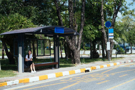 Black long hair college girl in uniform sitting at bus stop waiting for bus.の写真素材