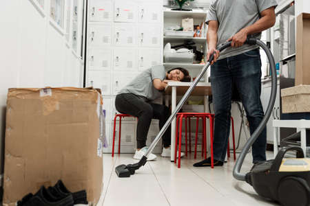 Husband cleaning the house using vacuum and let his wife sleep on the table.