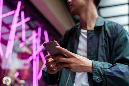 Cropped image of smartphone in a man's hands while he hold it in front of building with pink neon...