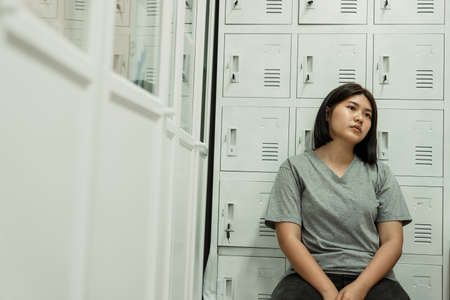 Sad tired young asian woman sitting in locker room.の写真素材