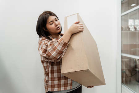 Strong asian woman carrying big box out of the house. Chubby asian woman lifting the box. Moving service.の写真素材