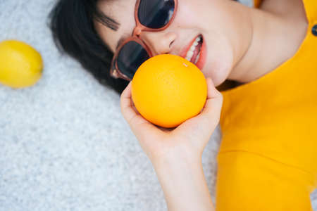 Close up portrait of woman wearing sunglasses holding orange. Summer vaction. Healthy fruit lover.