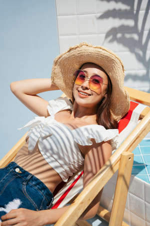 Beautiful young asian woman wearing straw hat and sunglasses laying on beach chair. Summer vacation.
