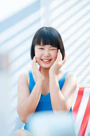 Portrait of Beautiful bob haircut asian woman in blue tank top shirt applying cream lotion on face.の写真素材