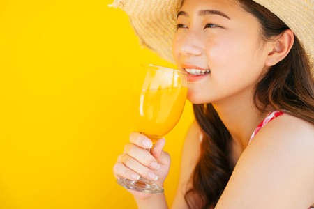 Close up beautiful young asian woman wearing hat holding orange juice glass cup isolated on orange...