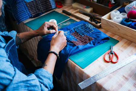 Cropped image of craftsman's hands while he sew the dark blue textile for fixing.