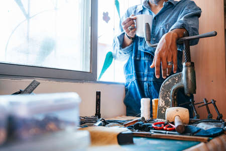 Low angle shot of a man in blue shirt standing at the window with white mug in his hand.