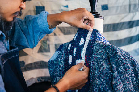 A man in blue shirt and apron measure the clothes on mannequin to make it fit, measure the back neck.の写真素材