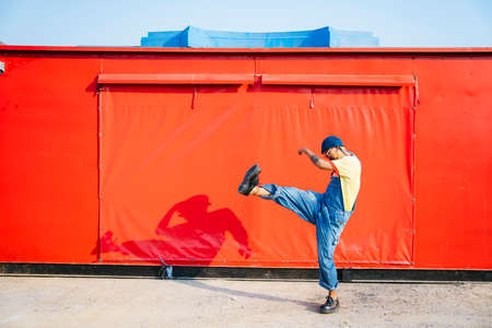 A man in yellow t-shirt and denim overalls standing and kick in front of the red trailer.の写真素材