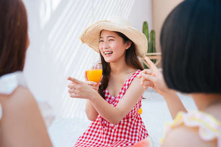 Beautiful young asian woman wearing hat and red dress drinking orange juice with friends in summer party.の写真素材