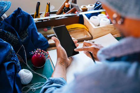 A man in blue clothes and hat find the reference of clothing pattern on the internet to get the...