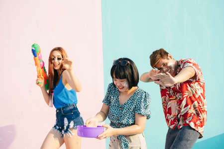 Songkran festival concept. Three people enjoy water festival in Songkran day. Isolated on pastel pink blue background. Portrait of three young thai people having fun in Songkran festival in Bangkok, Thailand.の写真素材