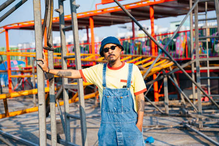 A man in yellow t-shirt and denim overalls standing in the abandoned amusement park in sunny day.の写真素材