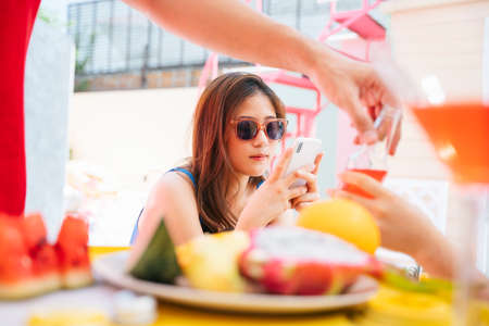 Beautiful asian woman wearing sunglasses sitting at bar in tropical island ordering juice from bartender.の写真素材