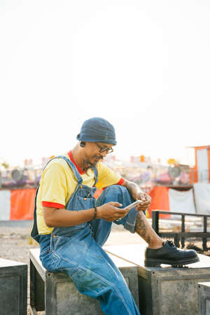 A man in yellow t-shirt and denim overall standing in the area of the abandoned amusement park.