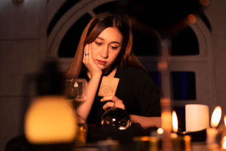 Beautiful young long hair woman fortune teller using tarot card to predict the future in dark room.