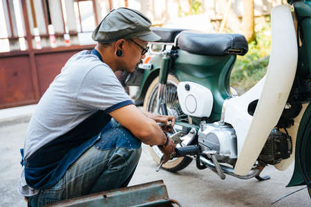 The mechanic fixing the motorbike, motorcycle, at his home by himself, use the tools from toolbox.