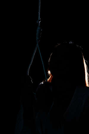 Silhouette portrait - Sad woman hanging herself with rope in dark room. Commit suicide.の写真素材