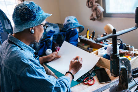 A man in blue clothes, hat and apron draw the pattern of his clothes on the paper with pencil and...