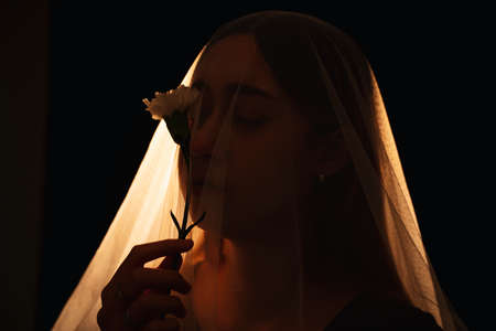 Beautiful mixed race woman holding white flower seal inside the bride viel. Wife ghost. Isolation over black background.の写真素材