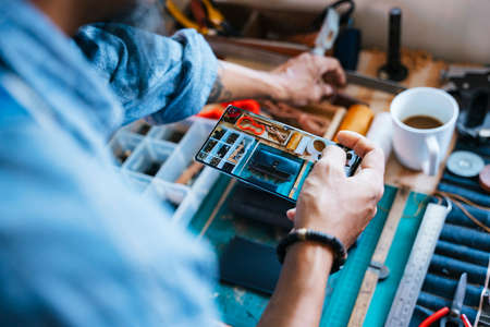 Cropped image of smartphone while the craftsman use it to take a photo of his handmade leather wallet for sell.の写真素材