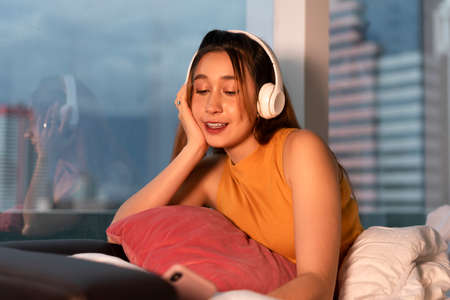 Beautiful mixed race woman enjoy listen to music with wireless headphone at night.の写真素材