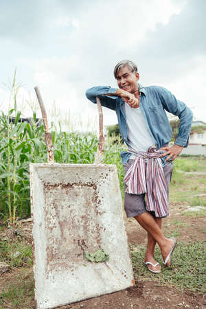 Asian elderly senior farmer standing with wheelbarrow cart in local farm.の写真素材
