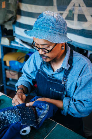 A man in blue clothes, hat and apron sew the fabric while cutting the clothes.の写真素材