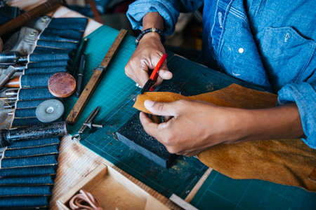 A man in blue shirt pick the scissors from tools bag to trim the leather.の写真素材