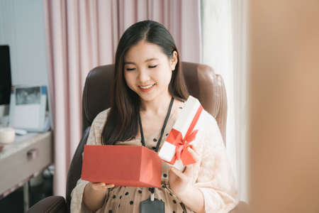 Beautiful pregnant asian businesswoman open a present gift box from husband.の写真素材