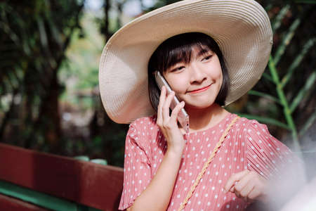 Beautiful asian thai woman short dark hair wearing a big hat using smartphone.の写真素材